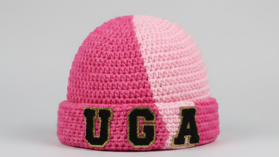Pink crocheted beanie with 'UGA' on a dark surface